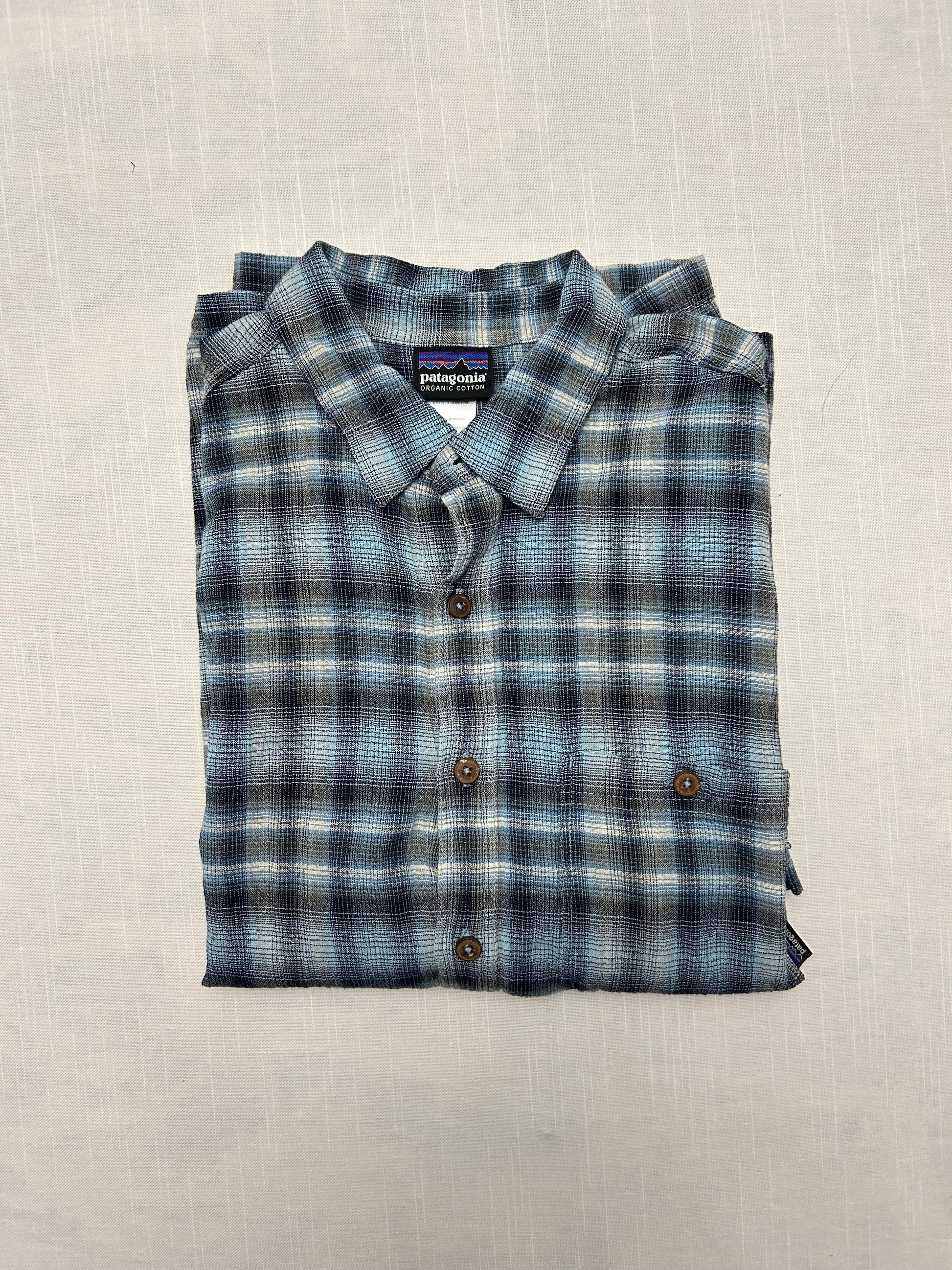 Folded blue and gray plaid shirt with a visible brand label on a beige background